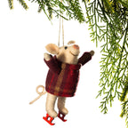 A plush mouse Christmas ornament wearing a red and brown plaid sweater and red ice skates, hanging from a string beneath evergreen branches against a white background.