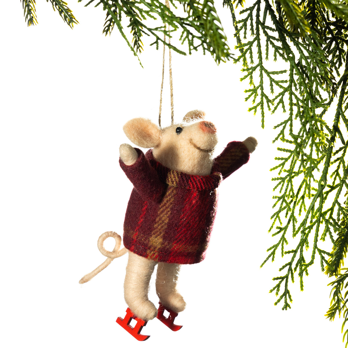 A plush mouse Christmas ornament wearing a red and brown plaid sweater and red ice skates, hanging from a string beneath evergreen branches against a white background.