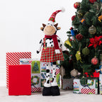A Christmas cow figurine standing around presents & a tree.