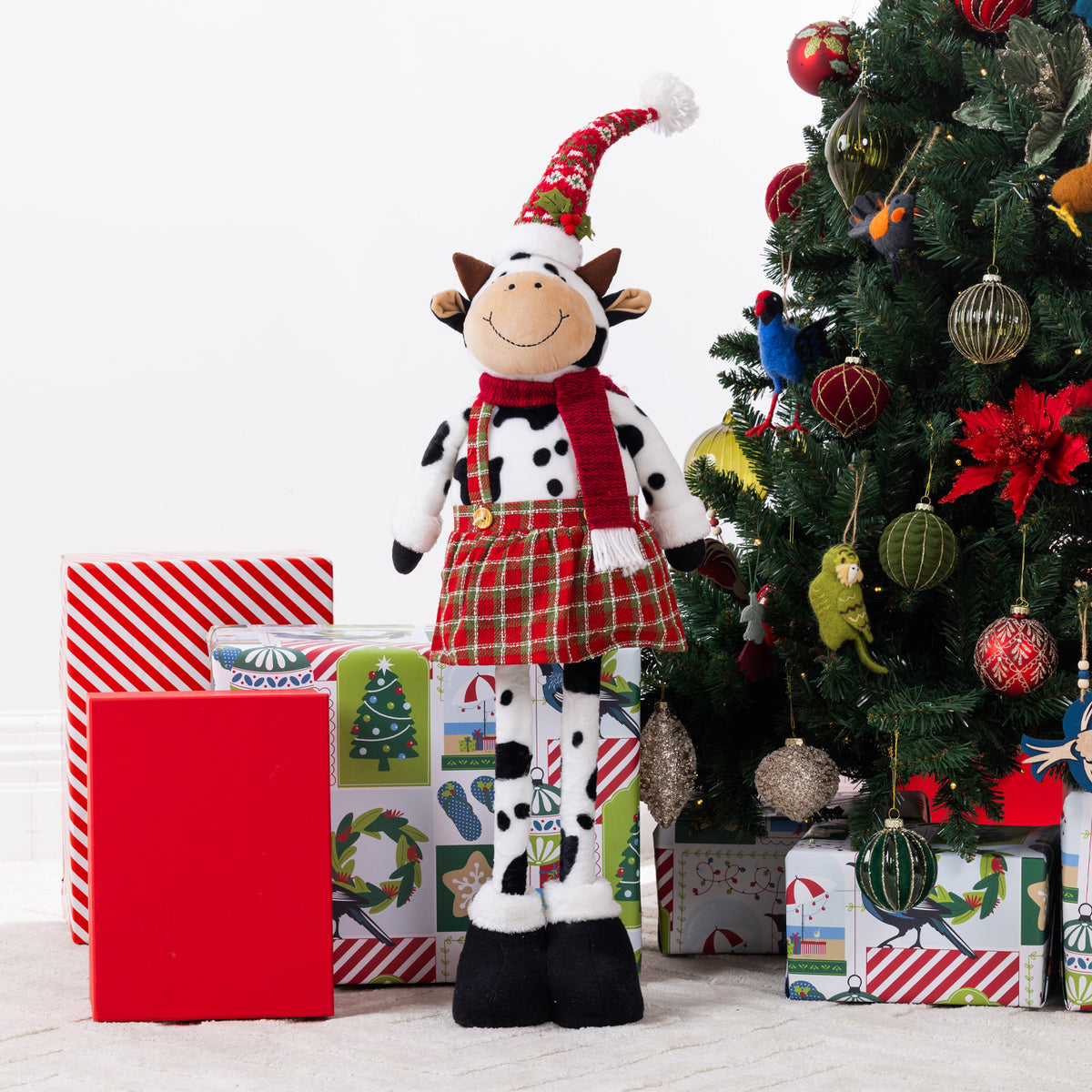 A Christmas cow figurine standing around presents & a tree.