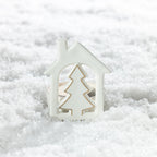 Front view of a white ceramic Christmas tree house tealight candle holder featuring a cut-out Christmas tree with gold edging, displayed in artificial snow.