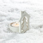 White ceramic Christmas tree house tealight candle holder with gold detailing and a lit tealight candle, nestled in artificial snow.