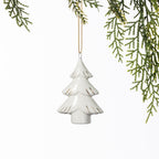 White ceramic Christmas tree hanging decoration with delicate gold detailing, suspended from a gold string amongst green foliage.