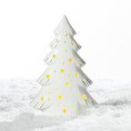 White ceramic Christmas tree LED decoration with glowing star and dot cut-outs and delicate gold detailing, displayed on a snowy surface.