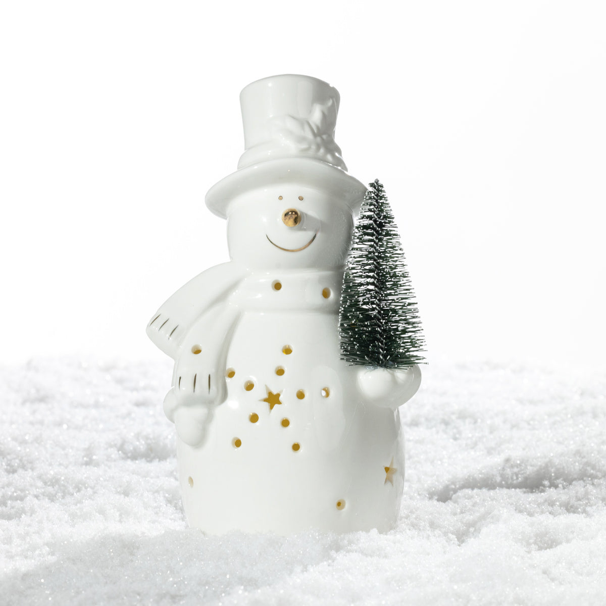 White ceramic snowman decoration with gold detailing and a miniature green Christmas tree, displayed on a snowy surface with its LED lights switched off.