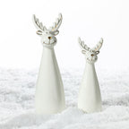 Two white ceramic Christmas reindeer decorations in different sizes, featuring smiling faces, gold-accented antlers and glossy finishes, displayed on a snowy surface.