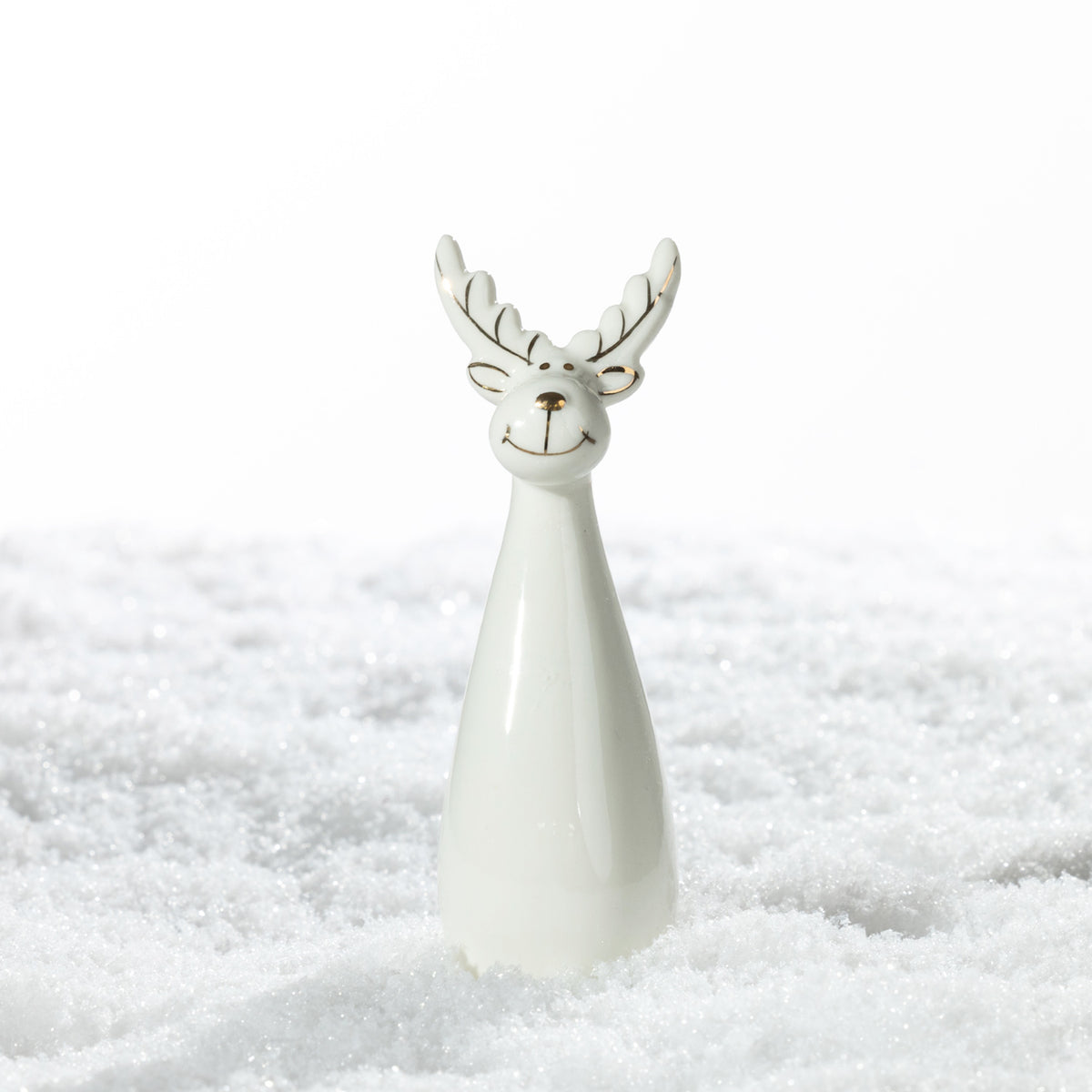Small white ceramic Christmas reindeer decoration with a smiling face, gold detailing and a tapered body, standing on a snowy surface.