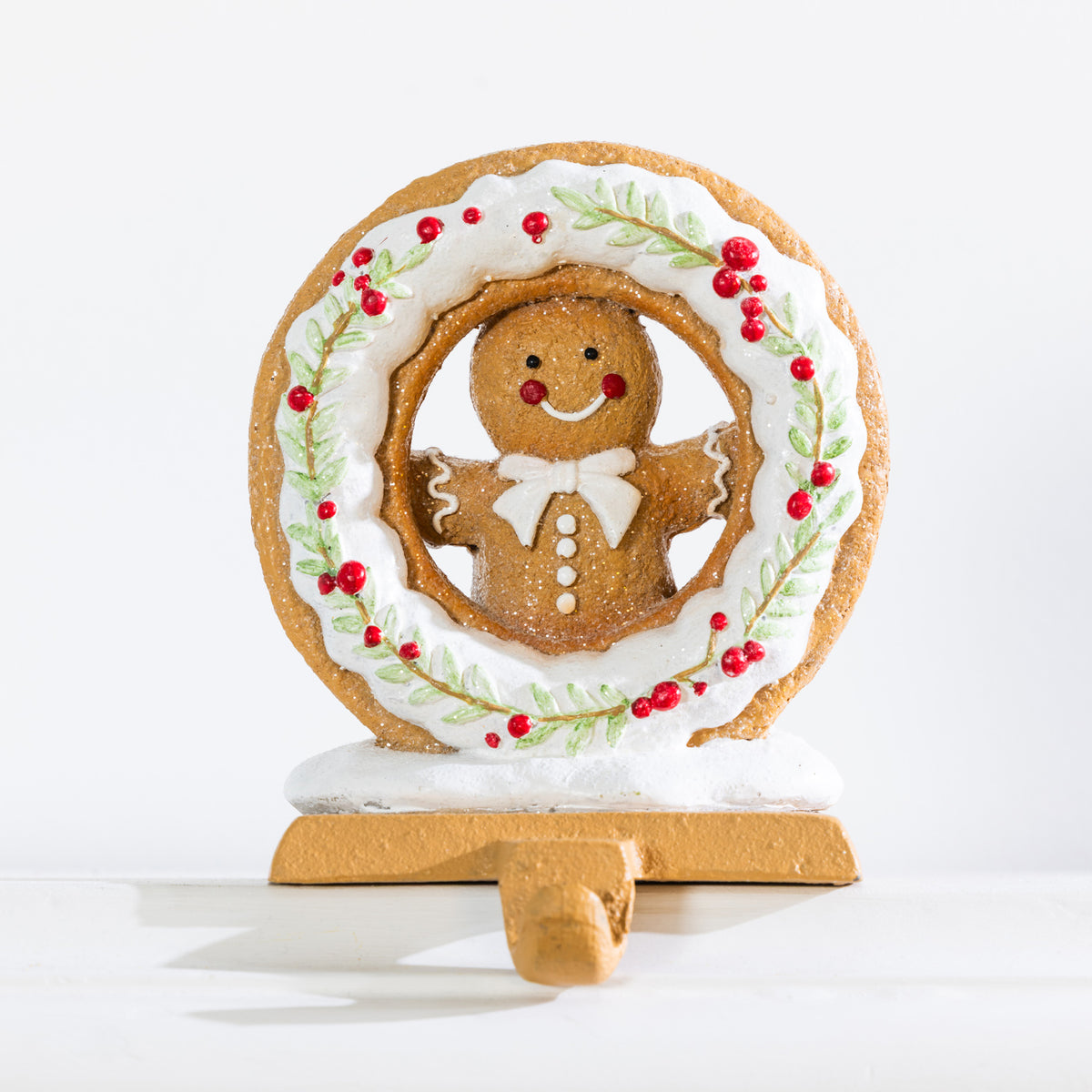 Gingerbread Christmas stocking holder featuring a smiling gingerbread man with white icing details, surrounded by a festive wreath decorated with red berries and green foliage.
