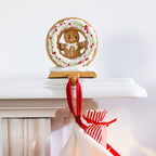 Close-up of a gingerbread Christmas stocking holder with white icing, red berries, green foliage and a red stocking hanging from its hook.