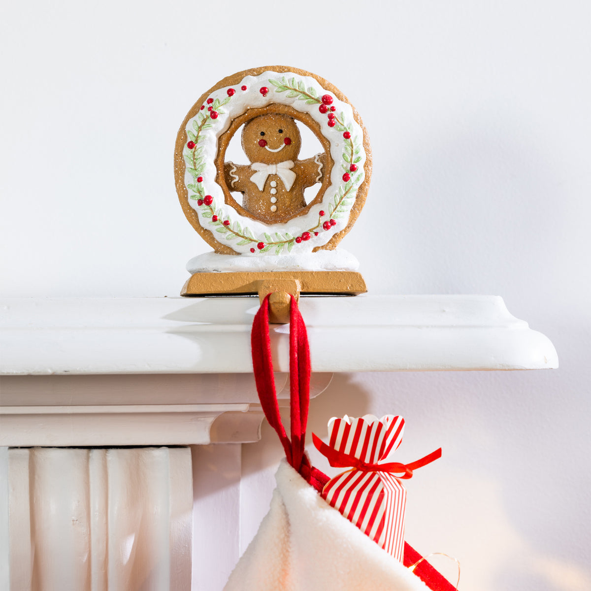 Close-up of a gingerbread Christmas stocking holder with white icing, red berries, green foliage and a red stocking hanging from its hook.