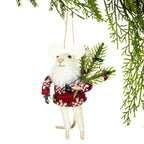 A white plush mouse Christmas ornament wearing a red and white knit sweater, holding a small evergreen branch with colorful ornaments, hanging against a white background with green pine branches framing the top right.