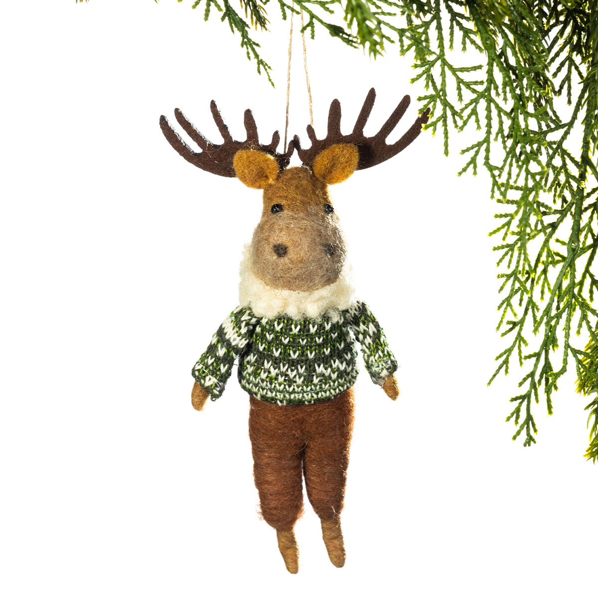 A felted wool moose ornament hanging from a pine branch against a white background. The moose has brown antlers, a brown face and legs, tan ears and hooves, and wears a green and white patterned sweater with a white faux-fur neck.