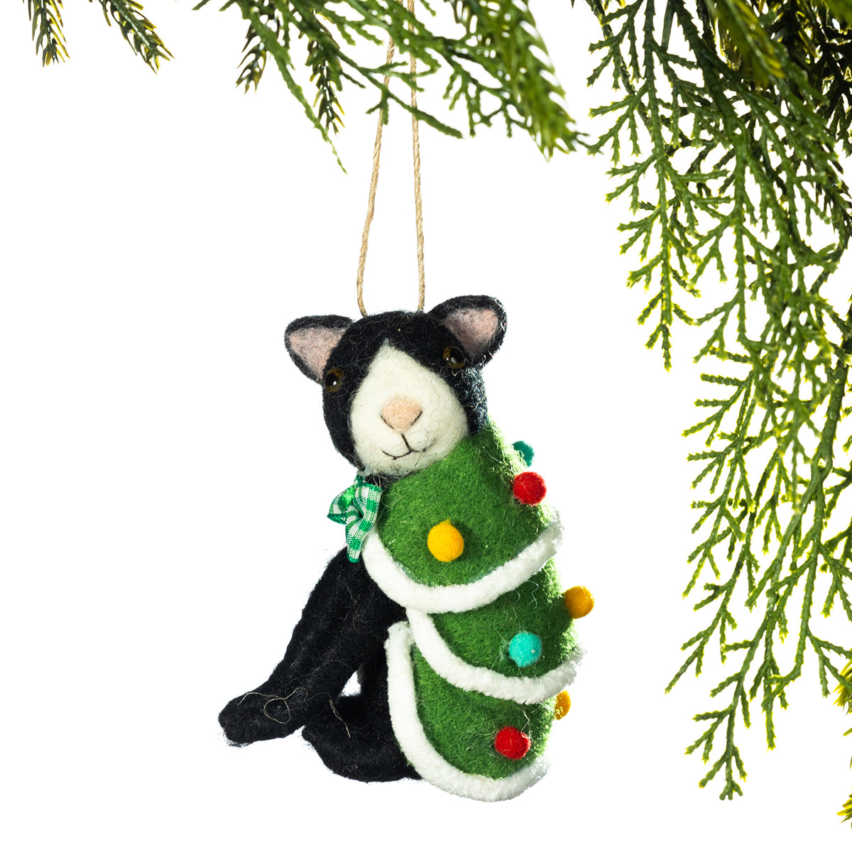 A handmade felt Christmas ornament shaped like a black and white cat wrapped in a green Christmas tree, hanging from a tree branch against a white background.