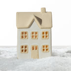 Large white ceramic Christmas house with a natural sand-coloured roof, chimney, two-storey design and detailed windows, displayed on a snowy surface.