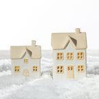 Small and large white ceramic Christmas houses with sand-coloured roofs, detailed windows and warm LED lighting, displayed together on a snowy surface.