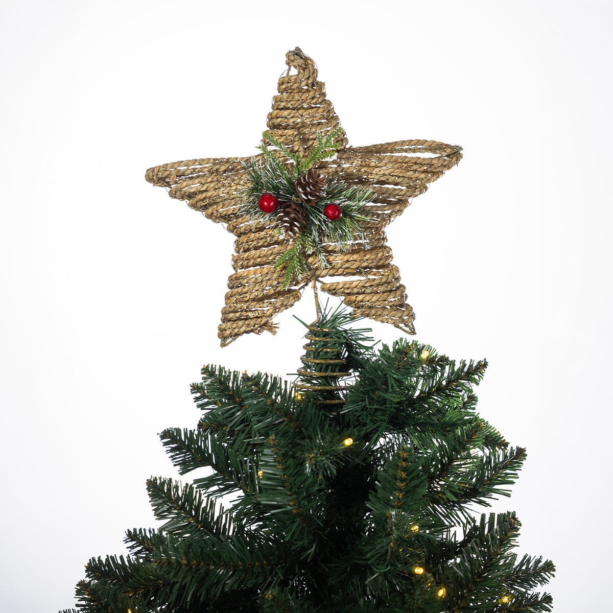 Christmas Wishes natural rattan star tree topper decorated with festive greenery, pinecones and red berries, displayed on top of a Christmas tree.