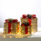 Three gold rattan present box LED decorations in different sizes, finished with red metallic bows, festive greenery and warm LED lights.