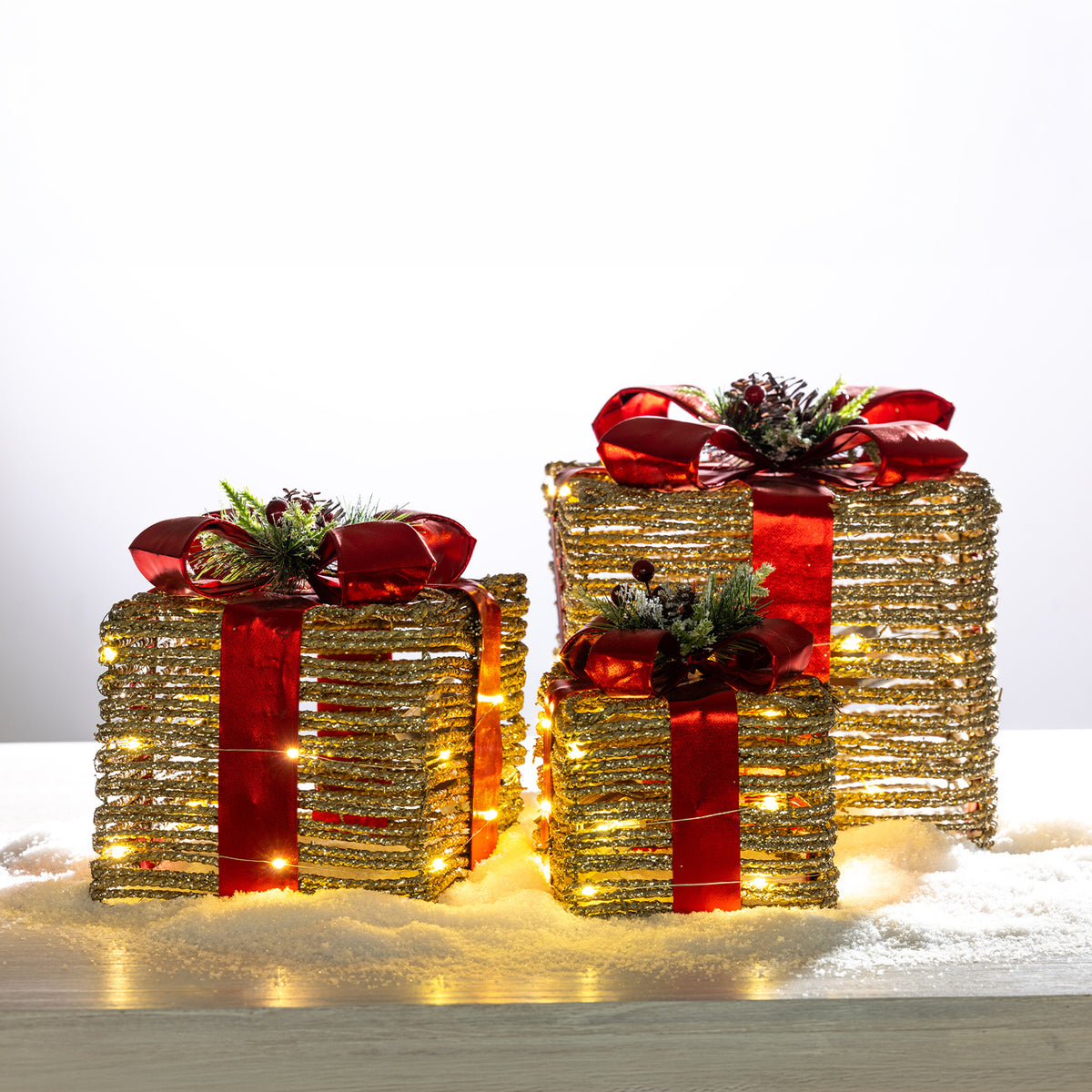 Three gold rattan present box LED decorations in different sizes, finished with red metallic bows, festive greenery and warm LED lights.