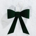 Christmas Wishes green velvet present bow with sparkling dot details and a hanging ribbon, displayed on a snowy background.