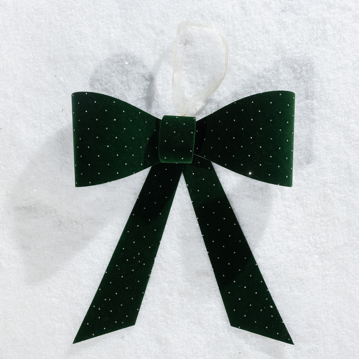 Christmas Wishes green velvet present bow with sparkling dot details and a hanging ribbon, displayed on a snowy background.