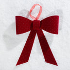 Christmas Wishes red velvet present bow with sparkling dot details and a hanging ribbon, displayed on a snowy background.