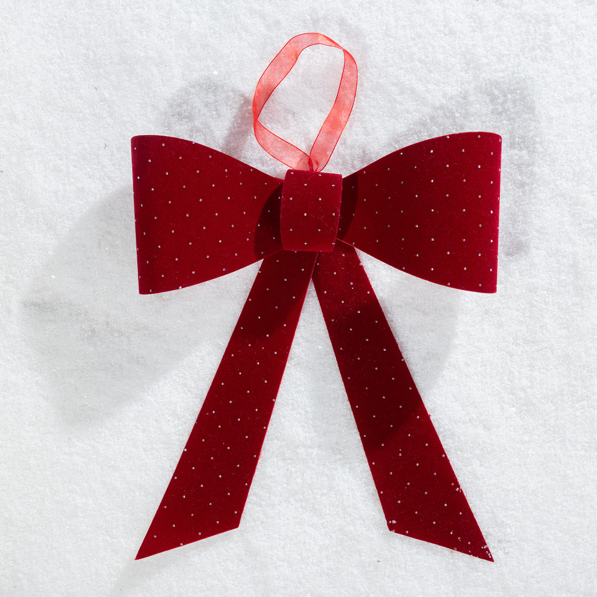 Christmas Wishes red velvet present bow with sparkling dot details and a hanging ribbon, displayed on a snowy background.