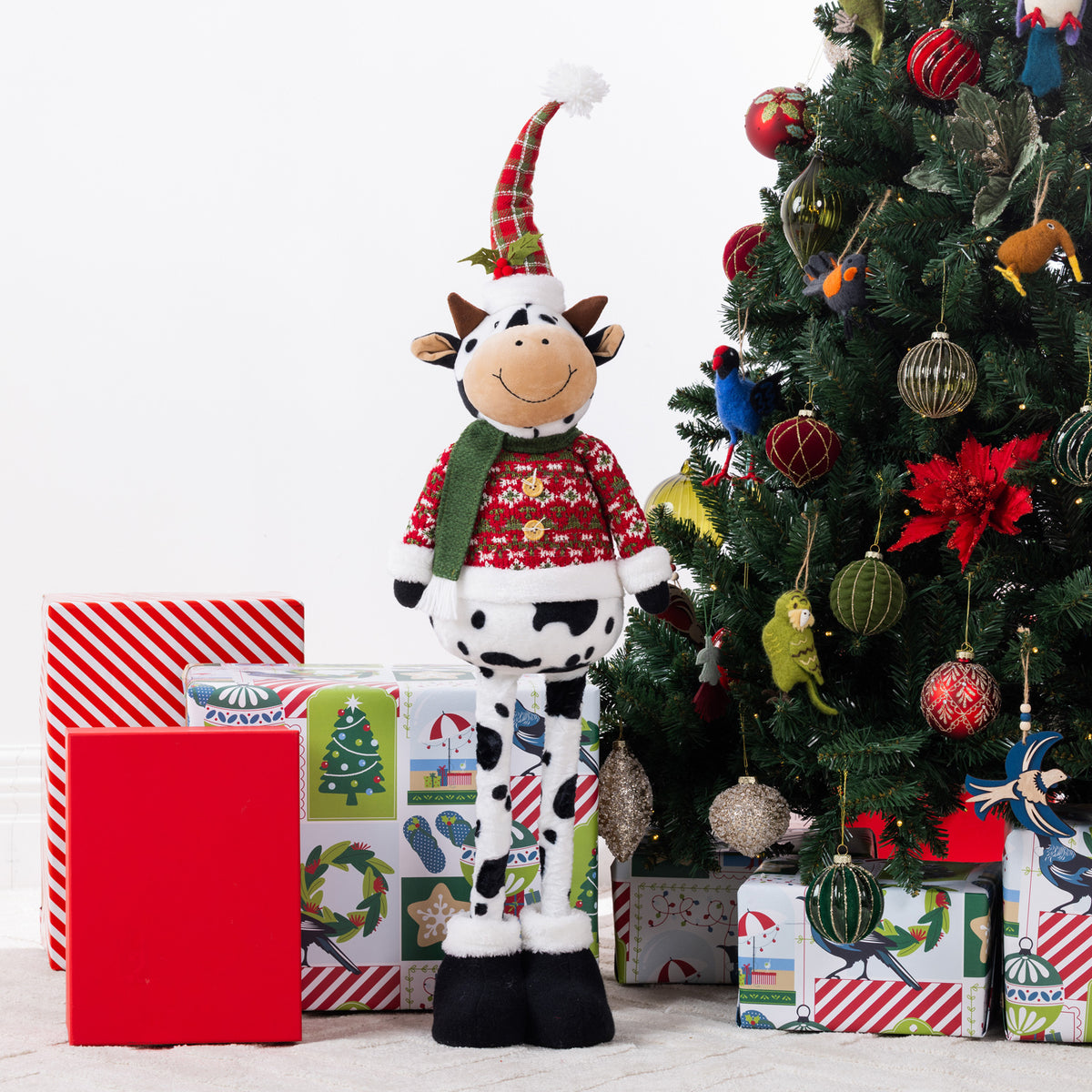 A Christmas cow figurine standing around presents & a tree.