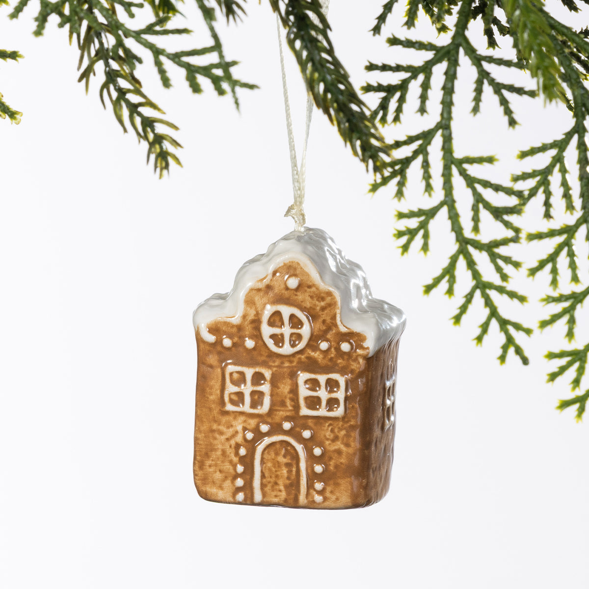 Gingerbread-style ceramic house hanging decoration with white frosted roof detailing, displayed hanging from a Christmas tree branch.