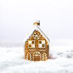 Gingerbread-style ceramic LED house with a snow-covered roof, snowflake detail and glowing windows, displayed in a snowy setting.