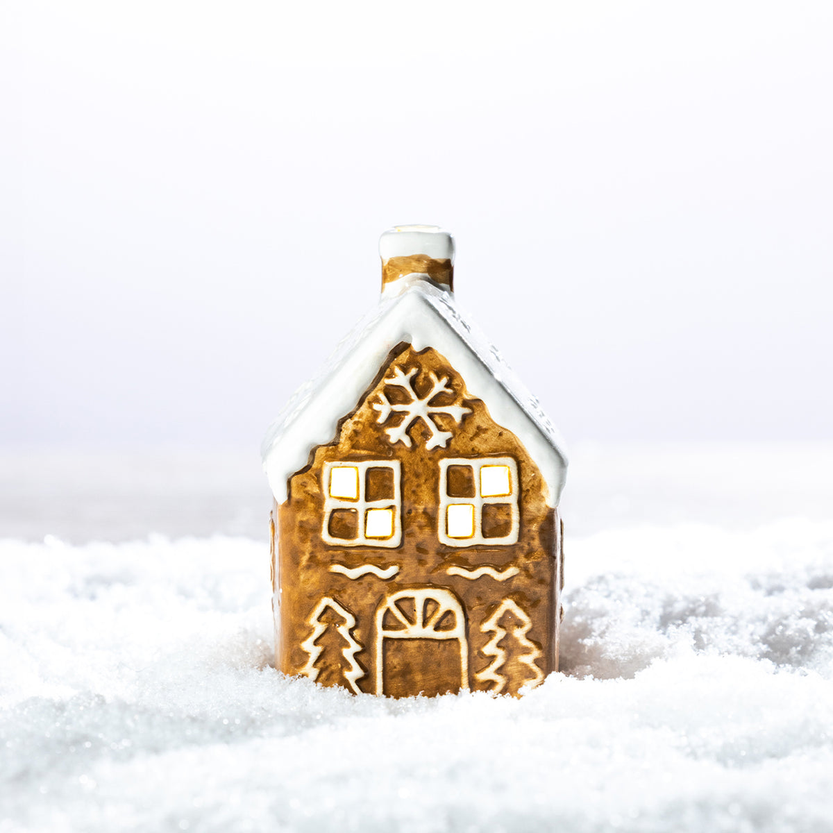 Gingerbread-style ceramic LED house with a snow-covered roof, snowflake detail and glowing windows, displayed in a snowy setting.