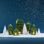 Christmas Wishes green ceramic village set illuminated among white snowy Christmas trees against a deep blue backdrop.