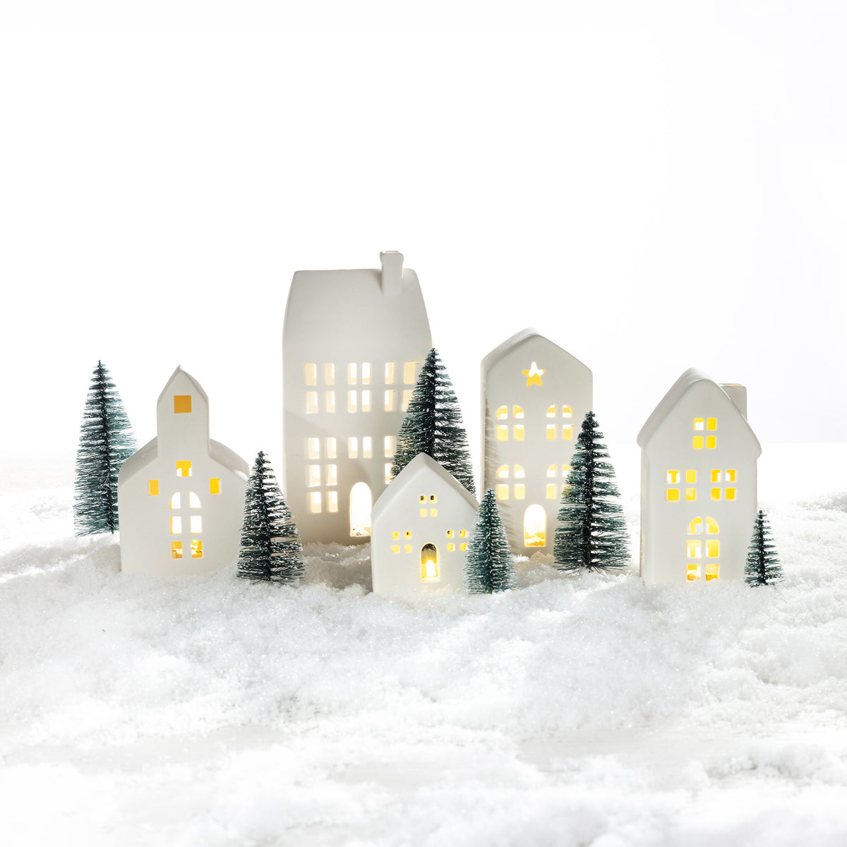 White ceramic Christmas village set with glowing houses and miniature evergreen trees arranged in a snowy festive scene.
