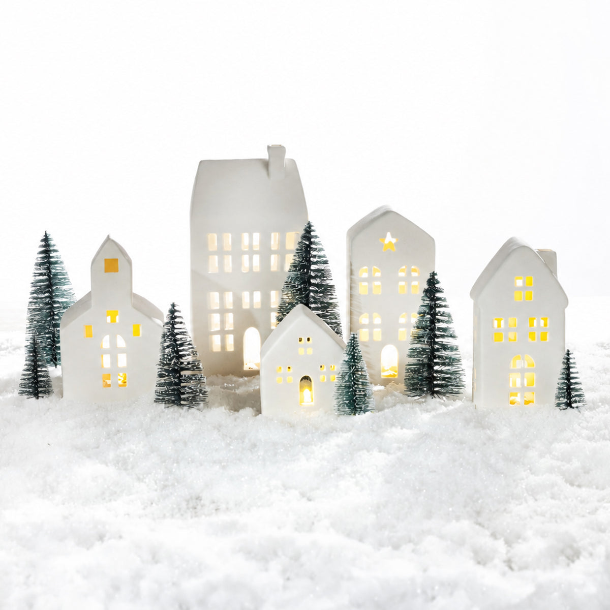 White ceramic Christmas village set with glowing houses and miniature evergreen trees arranged in a snowy festive scene.