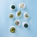 A collection of green, champagne and bronze glass Christmas baubles featuring glittered swirl and ribbed designs, displayed on a snowy light blue background.