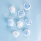 A collection of icy blue and white Christmas baubles featuring glittered snowflake, floral and scalloped designs, arranged on a snowy light blue background.