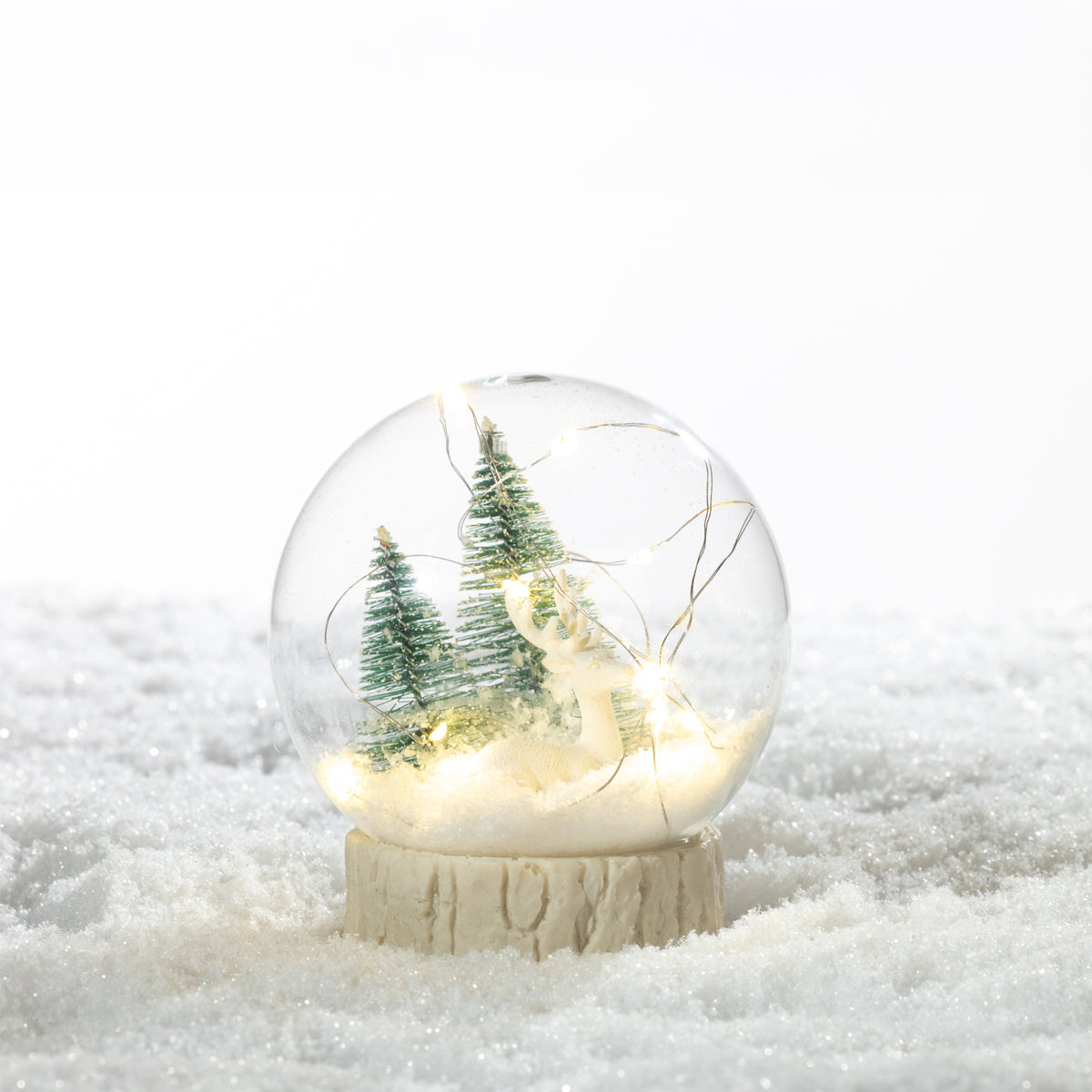 Christmas Wishes Christmas Tree Snow Globe LED Decoration Clear – Create a magical festive display with this clear Christmas snow globe LED décor. Featuring miniature Christmas trees and a reindeer surrounded by snowy detailing, warm LED lights illuminate the scene from within for a cosy seasonal glow. A charming piece for displaying on shelves, sideboards or festive table settings.