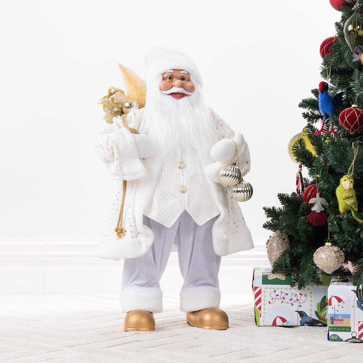 Christmas Wishes White & Gold Santa 80cm dressed in a white and gold festive outfit, holding gold decorations and silver baubles beside a decorated Christmas tree.