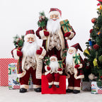Christmas Wishes traditional Santa figures in coordinating red tartan and cream outfits, displayed together with festive gifts and greenery beside a Christmas tree.
