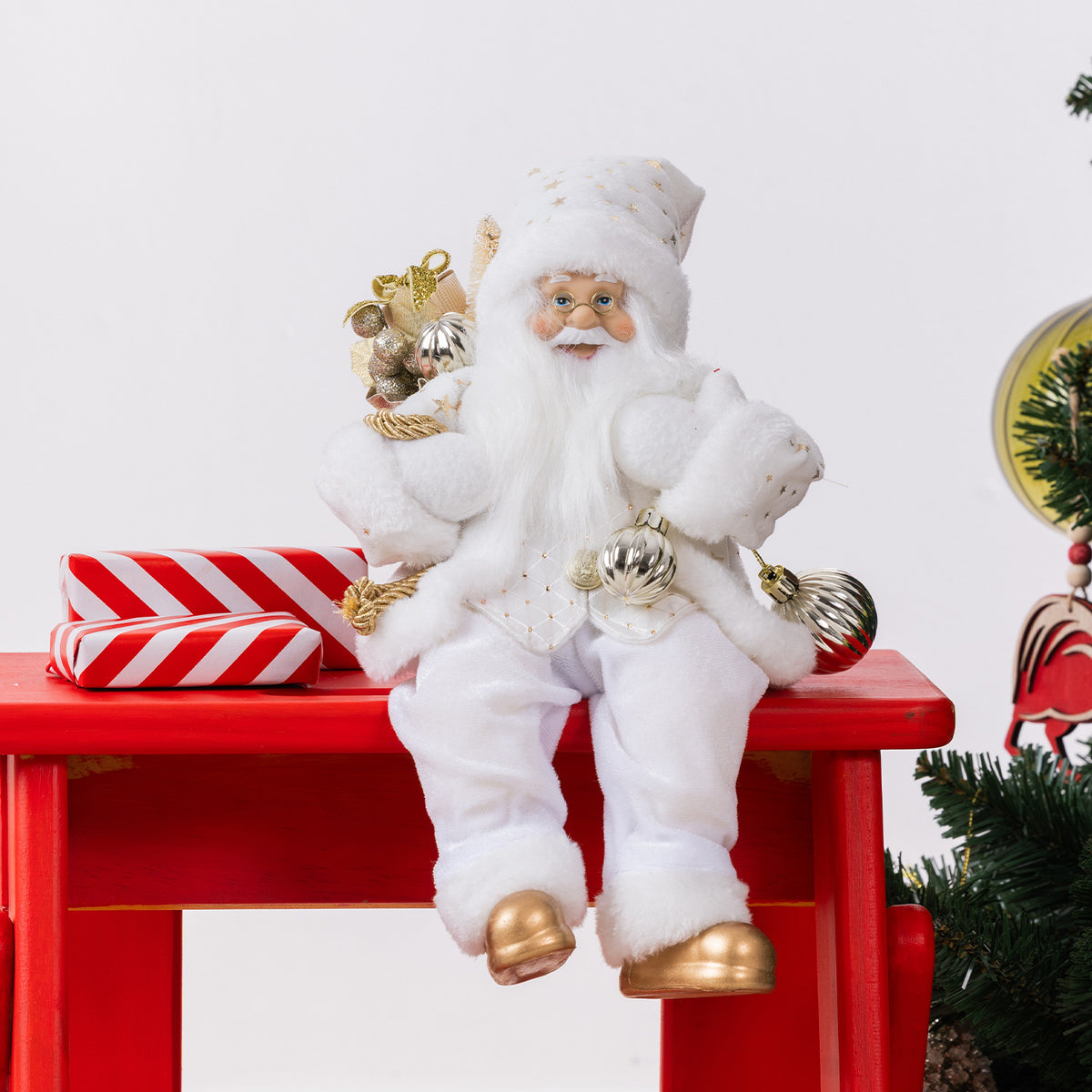 Christmas Wishes White & Gold Santa 80cm wearing a white and gold festive outfit, holding silver baubles and a sack of gold decorations beside a Christmas tree.