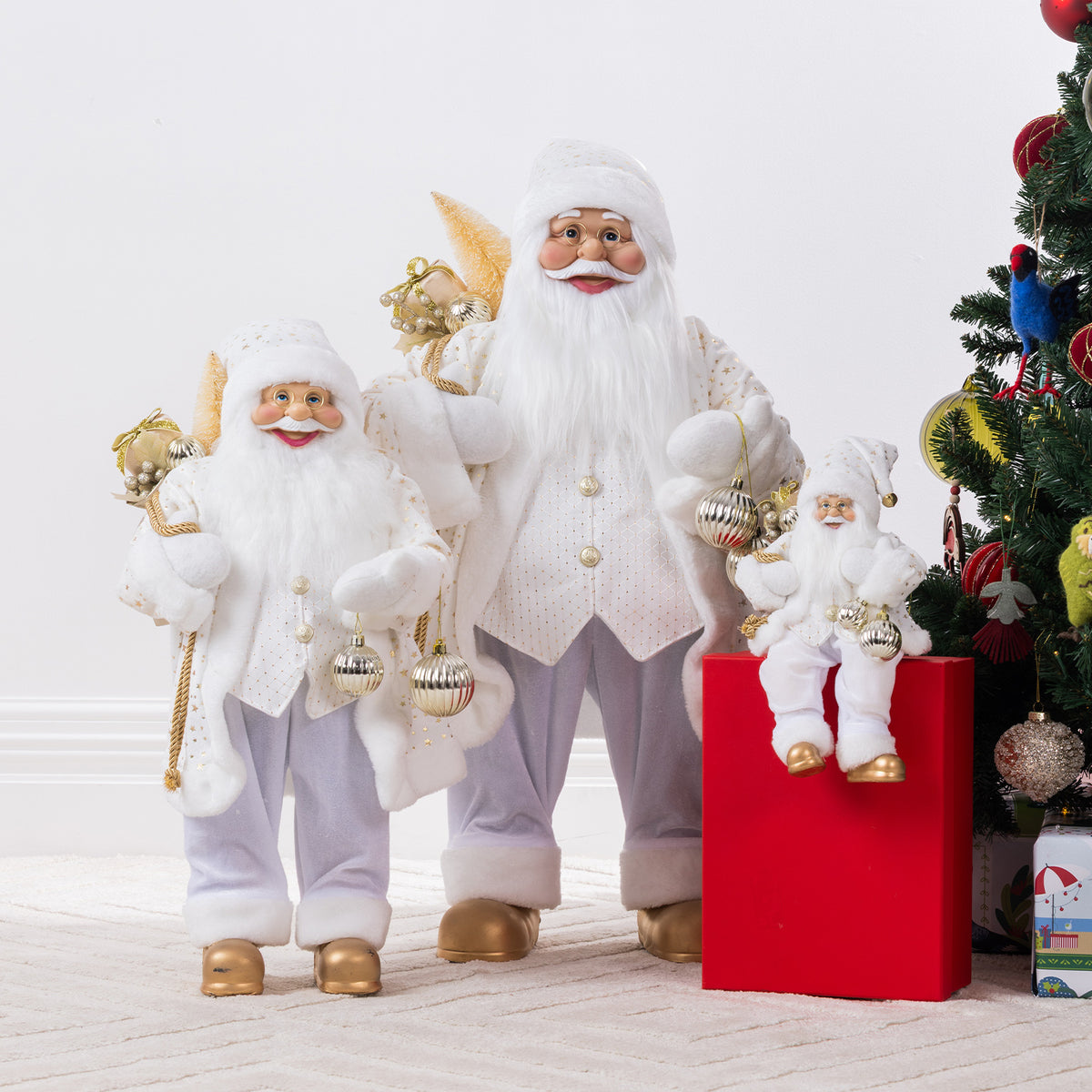 Three Christmas Wishes White & Gold Santa figures in different sizes, wearing matching festive outfits and displayed beside a decorated Christmas tree.