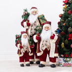 Three Christmas Wishes Red Traditional Santa figures in different sizes, wearing matching red tartan outfits and displayed beside a decorated Christmas tree.