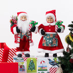 Christmas Wishes Gingerbread Mr and Mrs Claus figures dressed in festive red outfits, holding wrapped presents and displayed beside a decorated Christmas tree.
