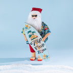 Christmas Wishes Summer Santa wearing a tropical shirt, red shorts, sunglasses and jandals while holding a colourful surfboard.