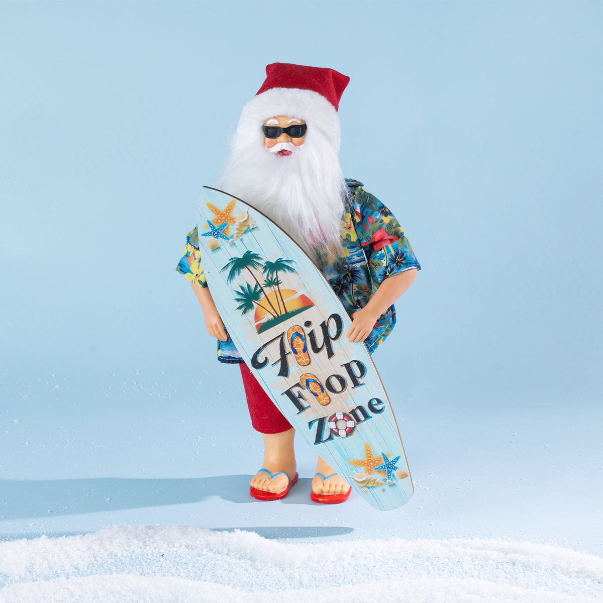 Christmas Wishes Summer Santa wearing a tropical shirt, red shorts, sunglasses and jandals while holding a colourful surfboard.