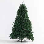 A pre-lit artificial Christmas tree with dense dark green needles on a black metal stand, photographed against a clean white studio background.