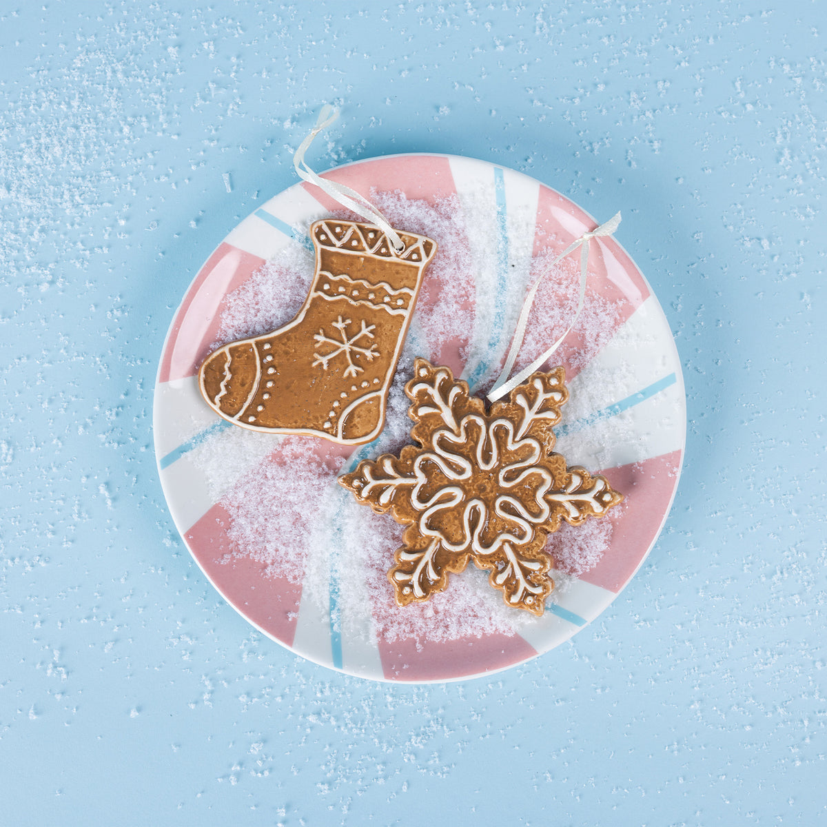 Pink and white peppermint swirl plate styled with gingerbread Christmas ornaments and scattered snow.