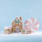Christmas Wishes gingerbread collection displayed on a snowy blue backdrop, featuring a gingerbread house mug, candy house cookie jar, peppermint plate and decorative houses.