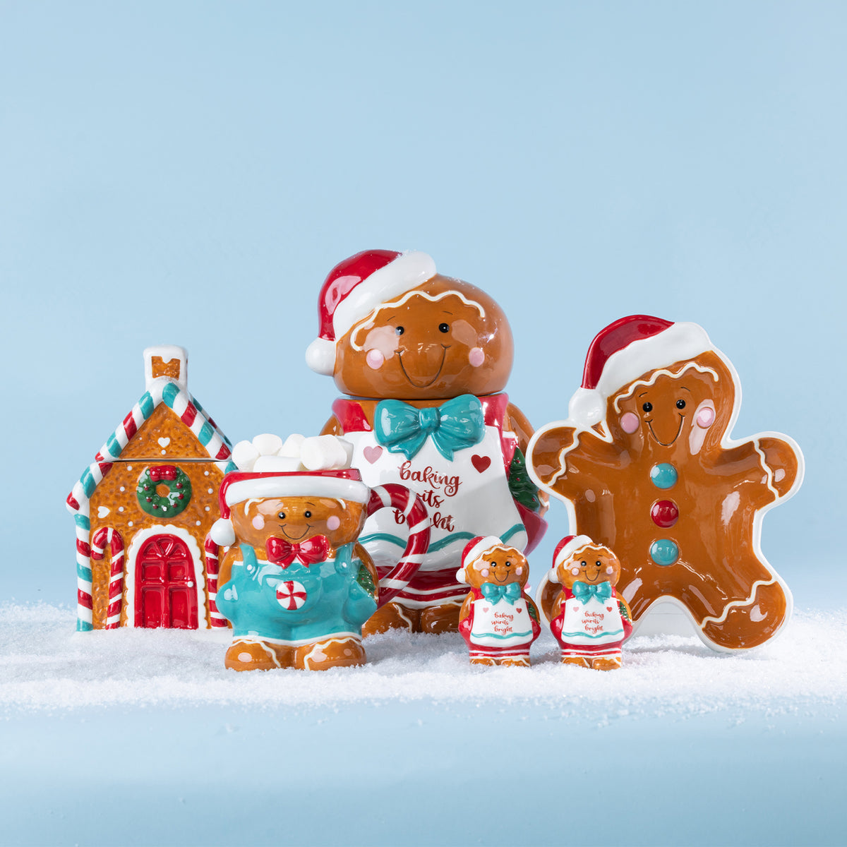Festive gingerbread collection displayed on snow, featuring a gingerbread house, mug, character decorations and gingerbread boy plate.