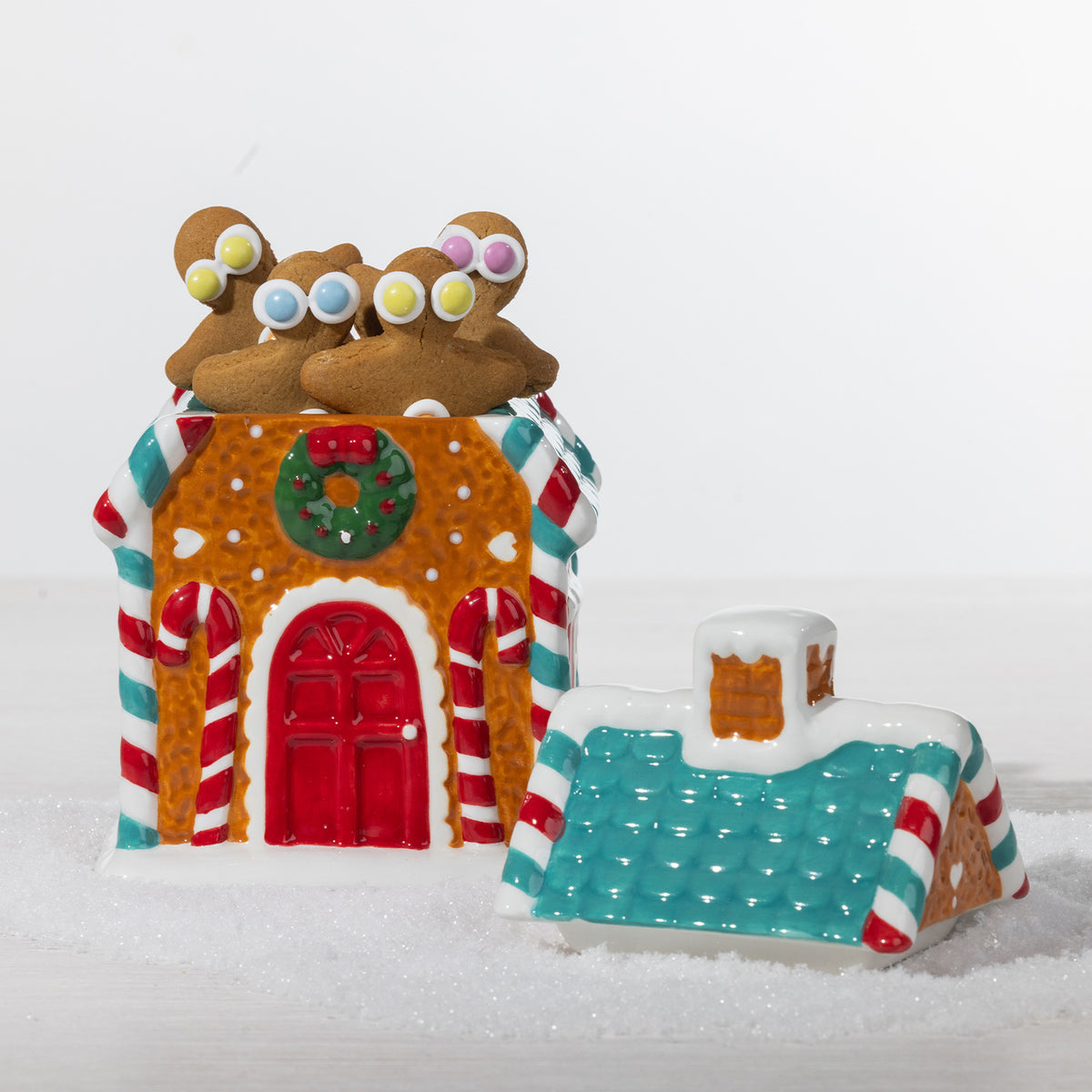 Gingerbread house cookie jar shown open and filled with gingerbread cookies, featuring candy cane details, a Christmas wreath and teal roof.