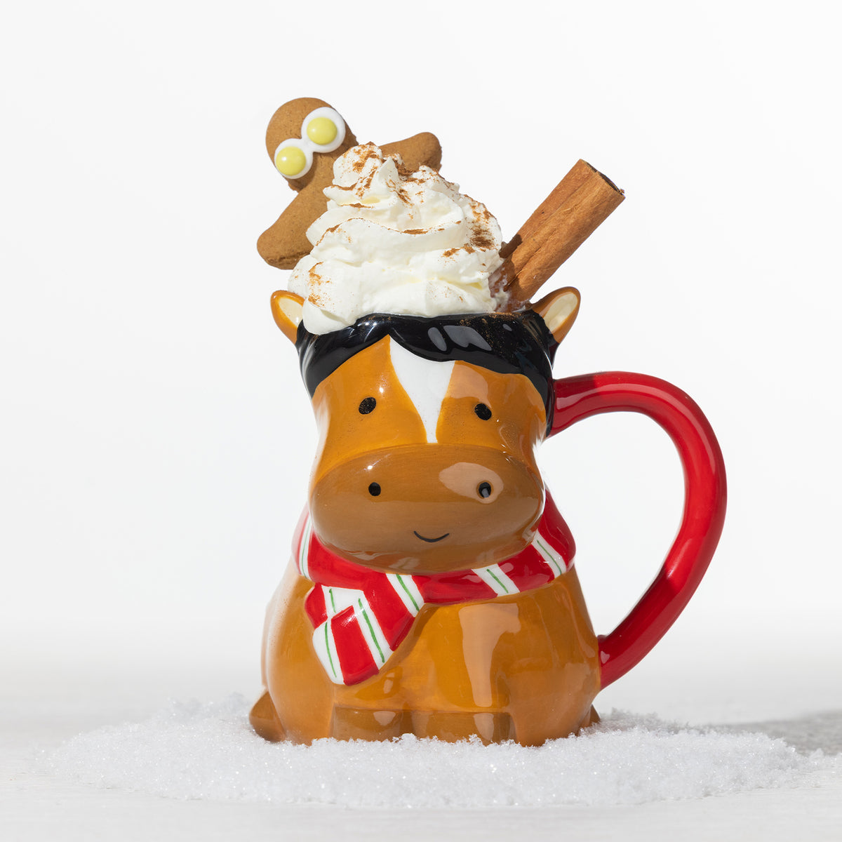 Christmas horse mug filled with whipped cream and a cinnamon stick, topped with a gingerbread figure and styled in a snowy festive setting.